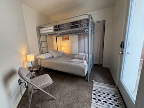 A bunk bed room with a desk, chair, lamp, and a door.