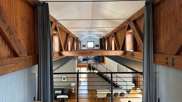 Un interior espacioso con vigas de madera a la vista, un nivel entre piso y vistas a un comedor inferior.