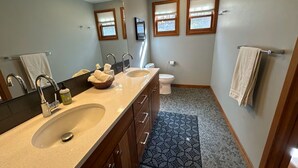 Un baño con tocador de doble lavabo, inodoro y ventana.