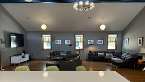 Amplia sala de estar con televisor grande, varias zonas de estar y una mesa de comedor.