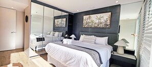 Une chambre moderne avec un grand lit, une table de chevet avec une lampe et une œuvre d’art accrochée au mur.