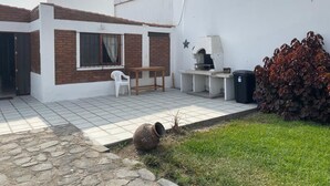 Uma casa moderna com um espaço de varanda que inclui um churrasqueira, uma parede branca e um pequeno jardim.