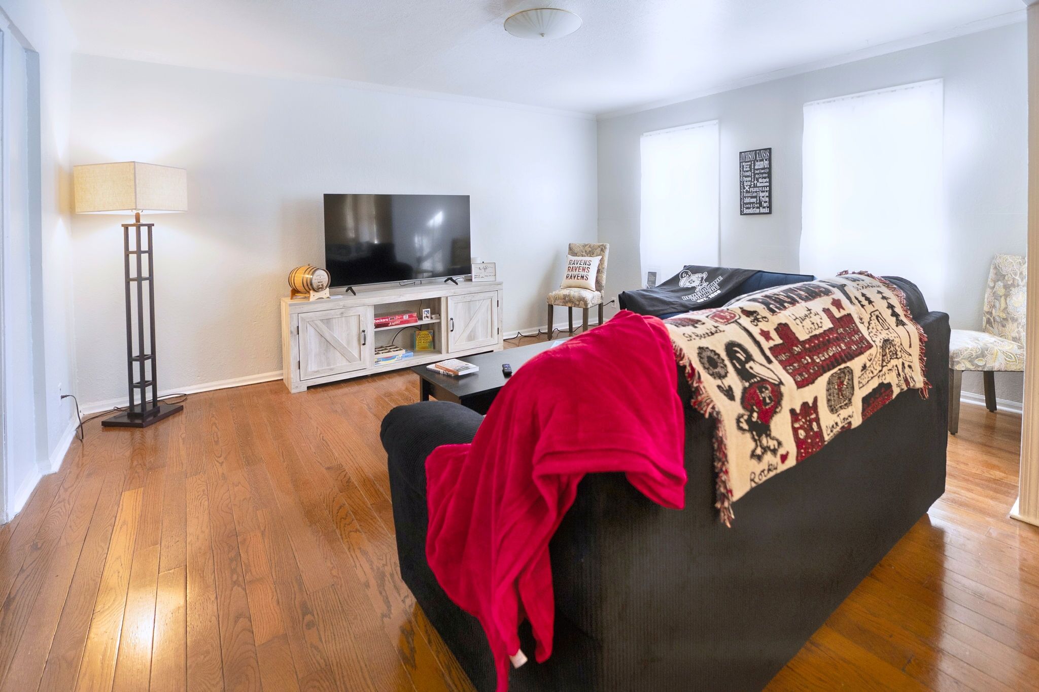 Ein Wohnzimmer mit einer schwarzen Couch, einer roten Decke, einem Fernseher auf einem Holzkasten und einer Stehlampe.