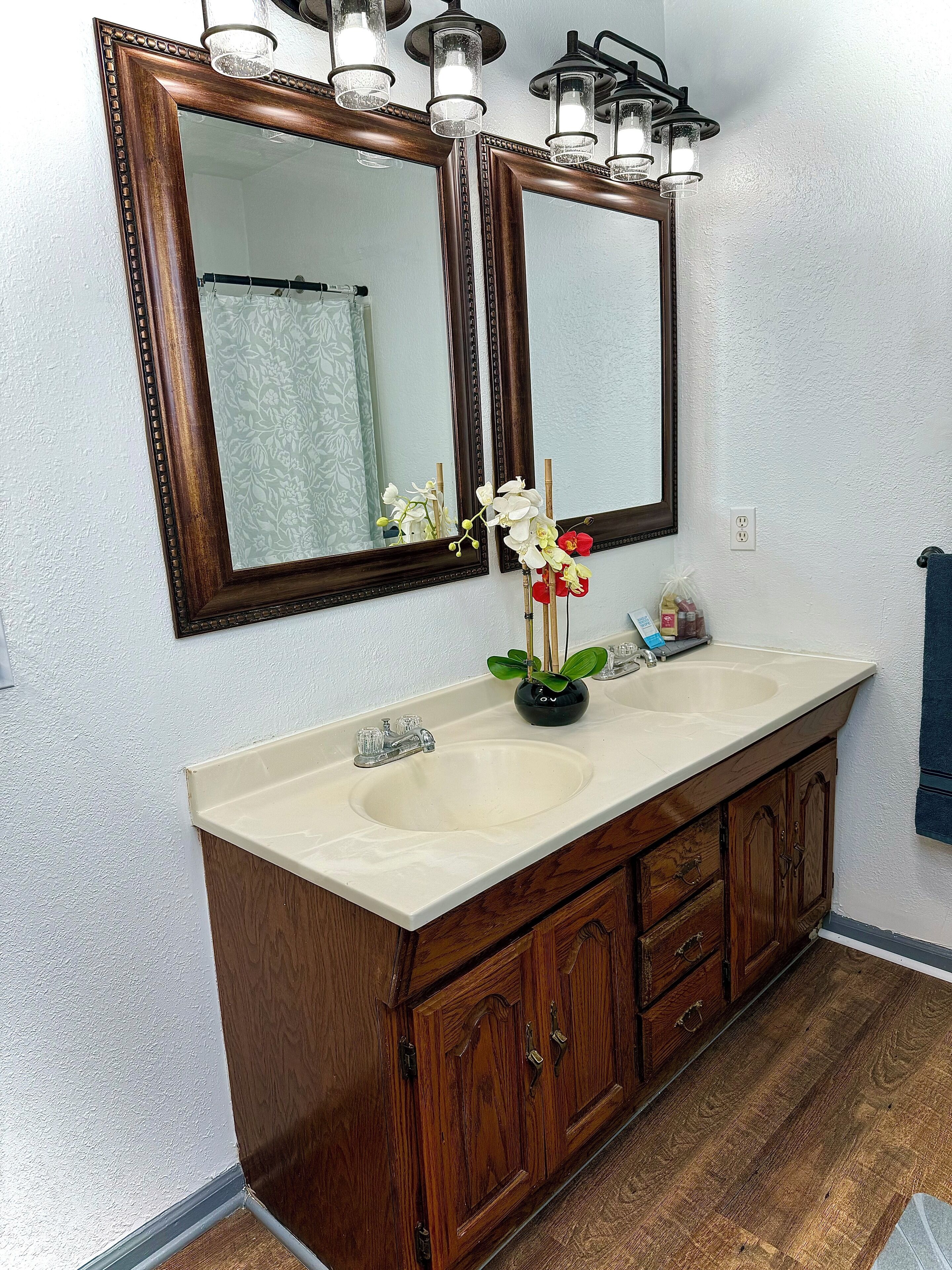 Un baño con tocador doble, dos espejos, un lavamanos y un florero con flores.