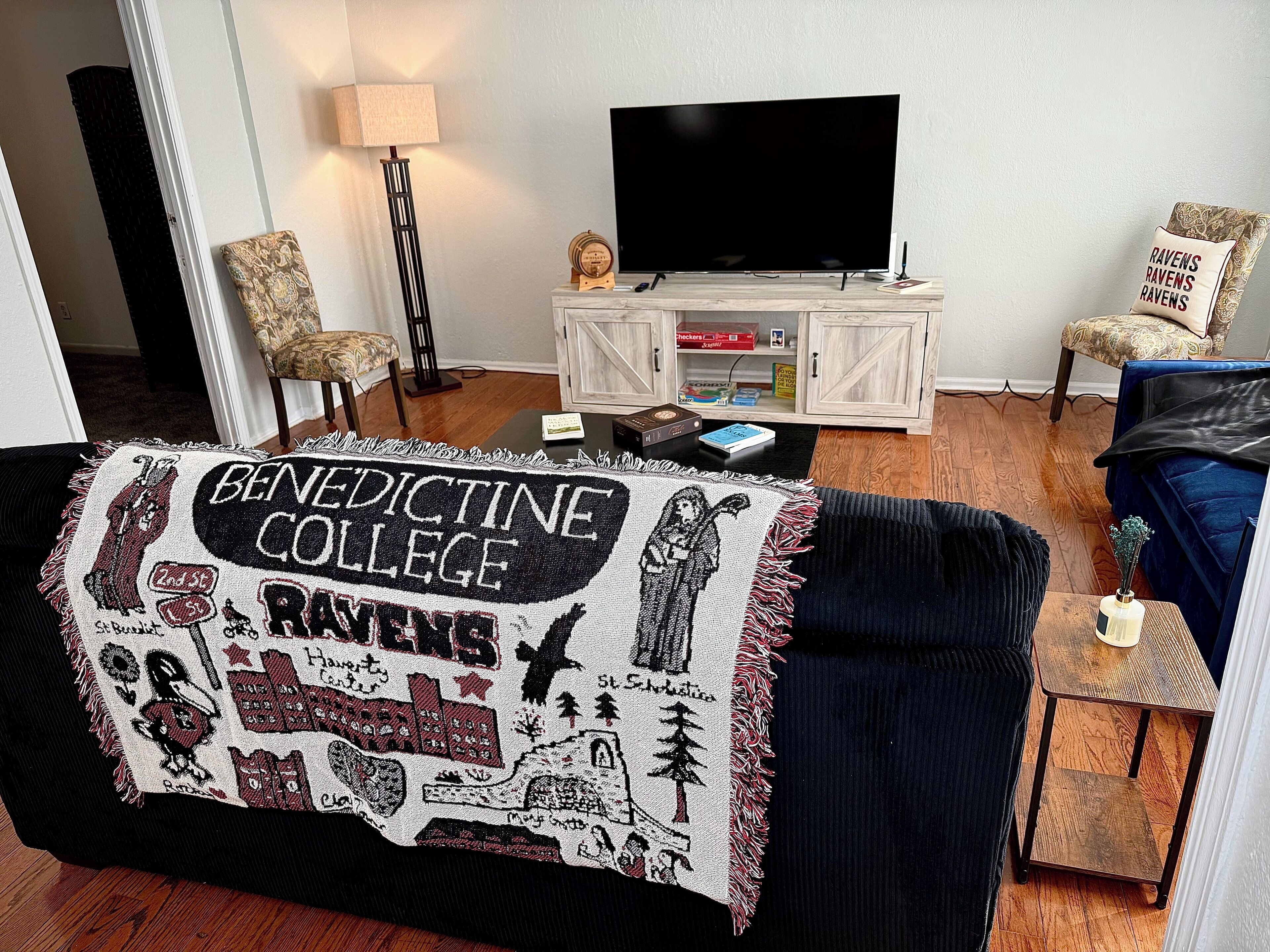 A living room with a dark blue sofa, a television on a wooden stand, and a patterned throw blanket.