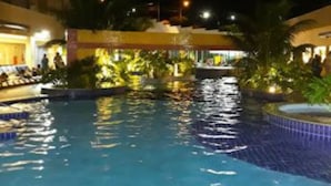 A nighttime view of a swimming pool with tiled edges, surrounded by buildings and palm trees. - Olimpia  Park Resort Ap.503C (Olímpia)