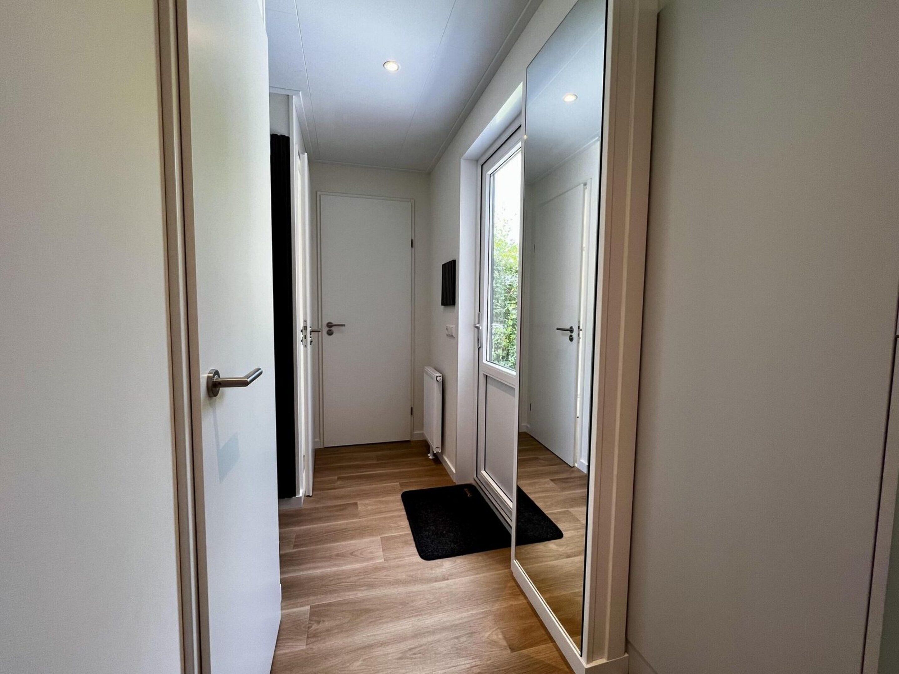 Un couloir avec un plancher en bois, des murs blancs et un paillasson noir.