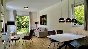 Un salon moderne avec un canapé, une table à manger et des chaises. Un téléviseur est fixé au mur, et il y a une fenêtre avec des rideaux.