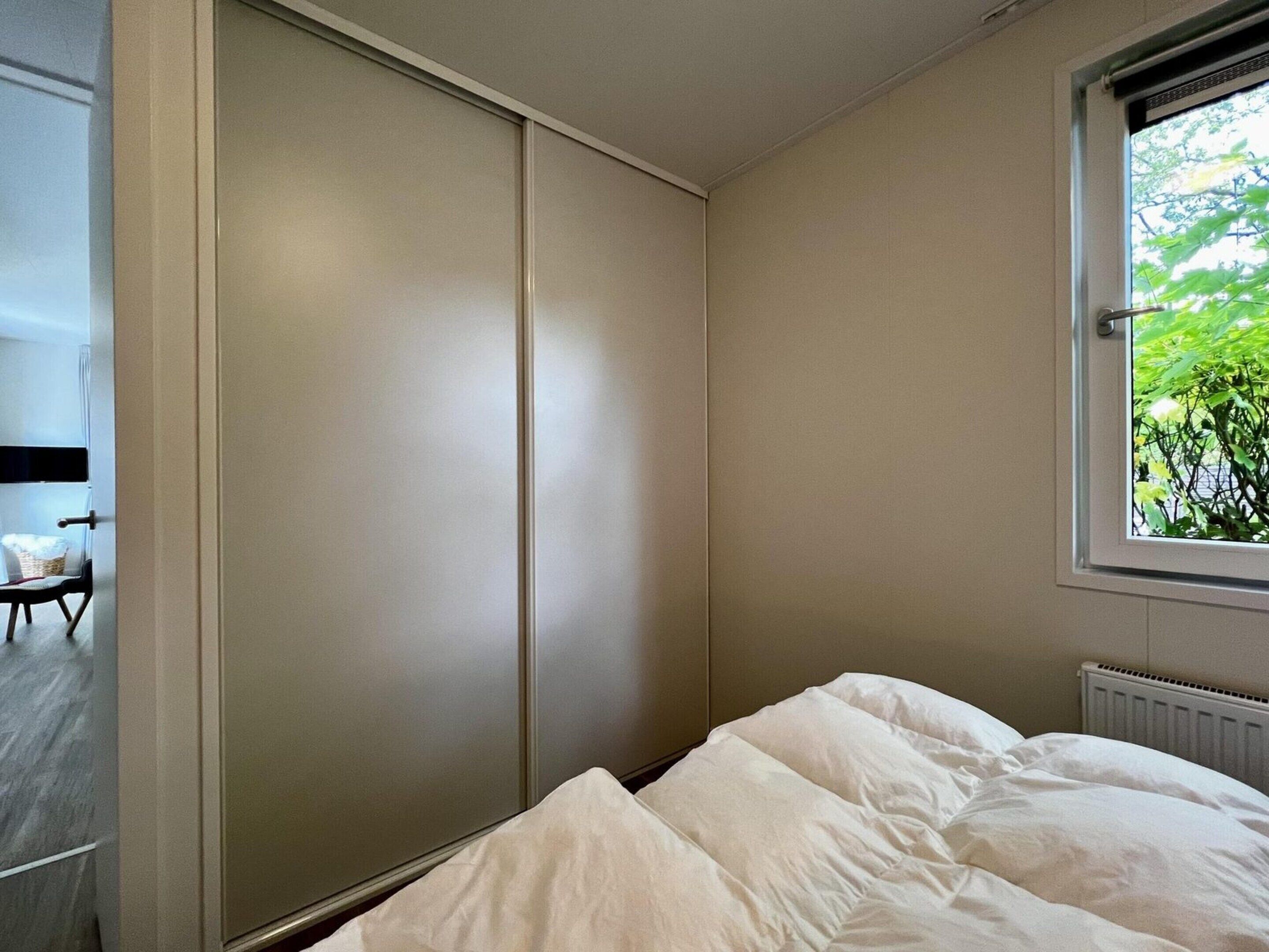 Ein Schlafzimmer mit einem Bett, einem Fenster mit Blick auf Grünflächen und einer Schiebetür.