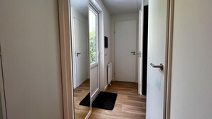 Un couloir doté de portes coulissantes en verre donnant sur une pièce, un paillasson noir et un mur blanc orné d’un petit objet noir.