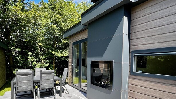 Une terrasse extérieure moderne, dotée d’une table et de chaises, d’un barbecue intégré et d’une porte-fenêtre coulissante donnant sur une terrasse.