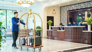 A hotel reception area with a reception desk, a gold-framed cart with luggage, and a reception counter with a logo.