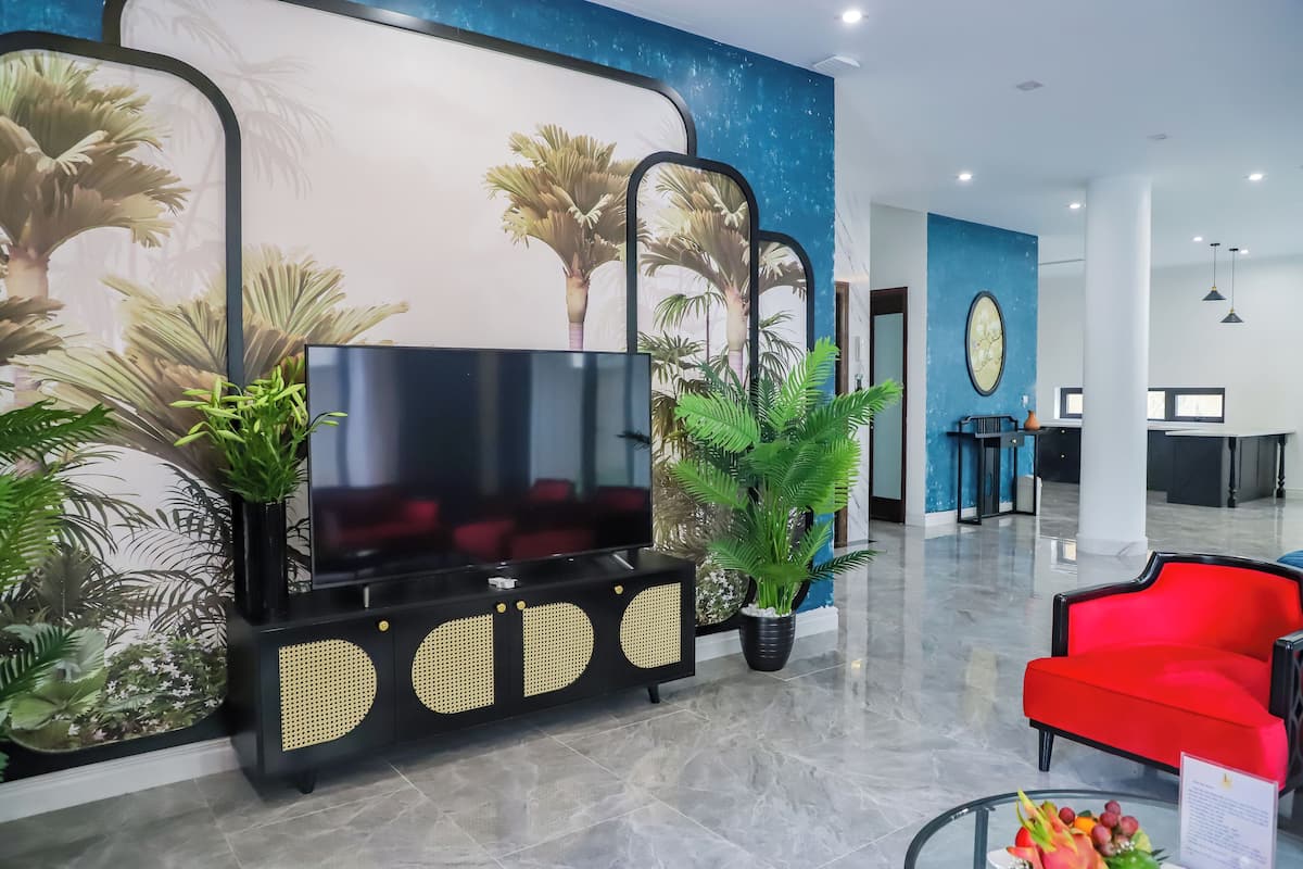 Eine moderne Lobby mit großem Fernseher, schwarzem Unterhaltungsmöbel, rotem Sofa und tropischer Wandkunst.