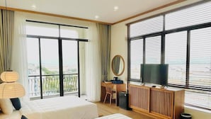 A hotel room with two beds, a desk, a television, and large windows.