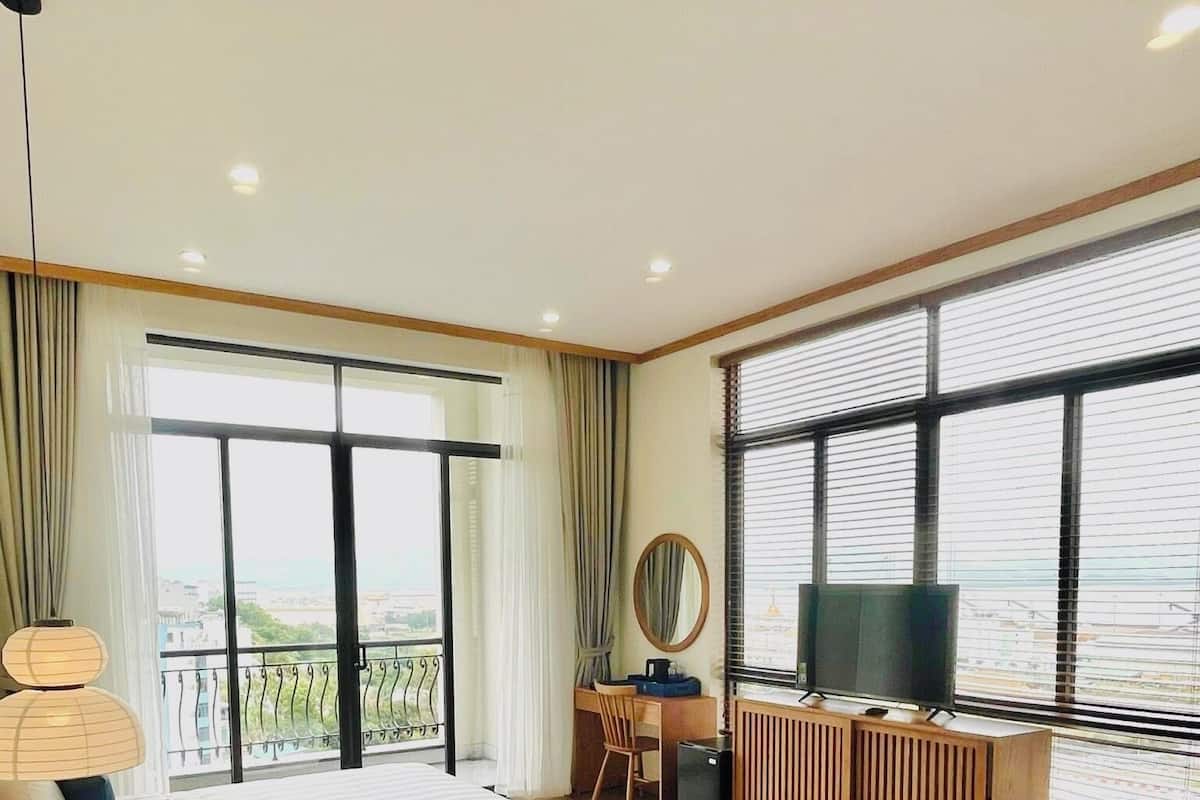 Ein Hotelzimmer mit zwei Betten, einem Schreibtisch, einem Fernseher und großen Fenstern.