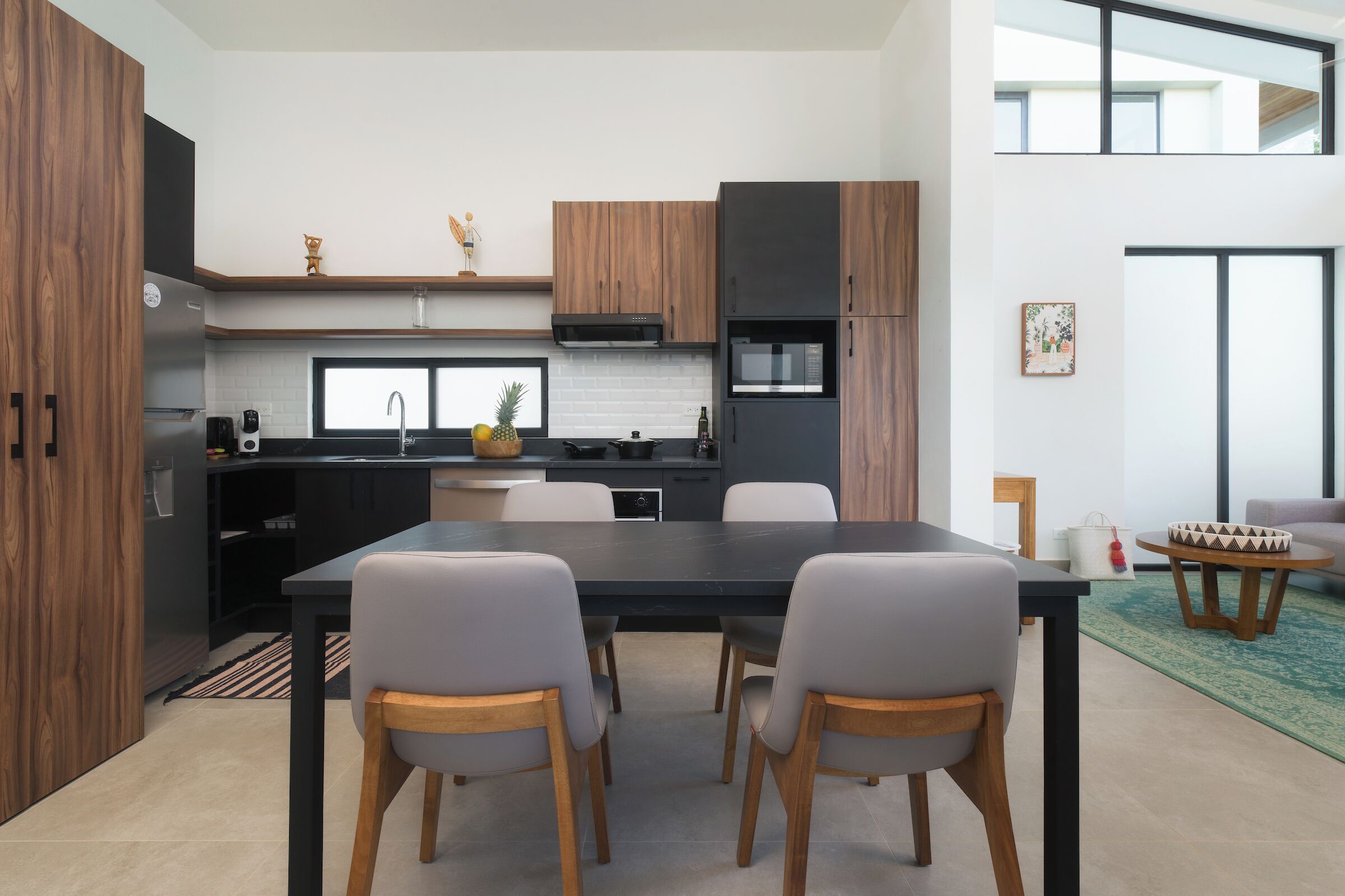 Une cuisine moderne avec des meubles de couleur sombre, un plan de travail noir et un coin repas comprenant une table et des chaises.