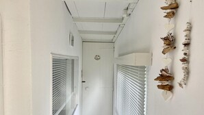 A narrow hallway with white walls and a wooden ceiling. There are two doors with white blinds, one on each side. A decorative string of seashells hangs on the right wall. - Furnished Chalet in Sint Maartenszee (Sint Maartensvlotbrug)