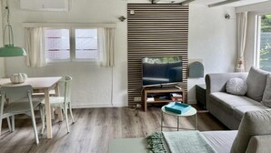 A living room with a TV, sofa, and dining area. - Furnished Chalet in Sint Maartenszee (Sint Maartensvlotbrug)
