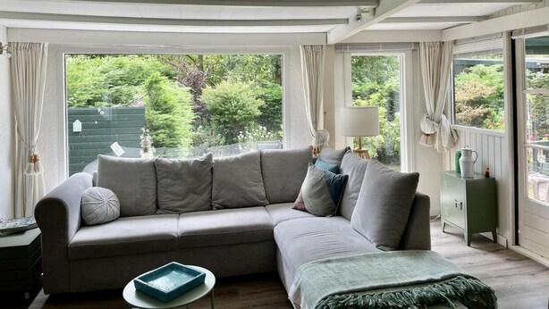 A modern living room with a grey sectional sofa, a small round table, and a green throw blanket. - Furnished Chalet in Sint Maartenszee (Sint Maartensvlotbrug)