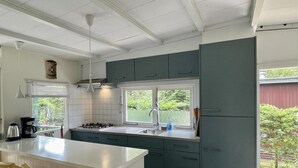 A modern kitchen with a central island, white countertops, and dark cabinets. There is a window providing natural light and a view of greenery outside. - Furnished Chalet in Sint Maartenszee (Sint Maartensvlotbrug)
