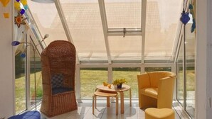 A modern room with a large glass window, wicker chair, yellow sofa, and a small table with a plant. - Holiday Home Near Dutch Beach and Dunes (Sint Maartensvlotbrug)