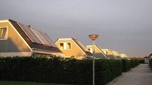 A row of modern, single-story houses with sloped roofs and solar panels, lined with a hedge and a paved walkway. - Holiday Home Near Dutch Beach and Dunes (Sint Maartensvlotbrug)