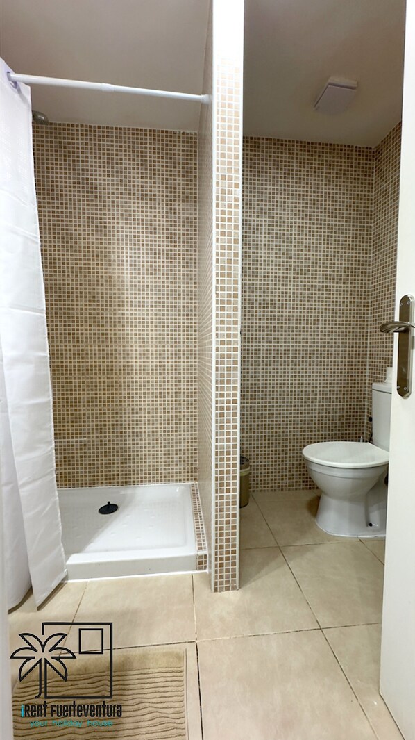 Un baño con ducha, inodoro y paredes de azulejos.