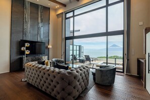 A modern living room with a large window, a tufted sofa, a flat-screen TV, and a view of a mountain. - Fuji Seiran (Numazu)