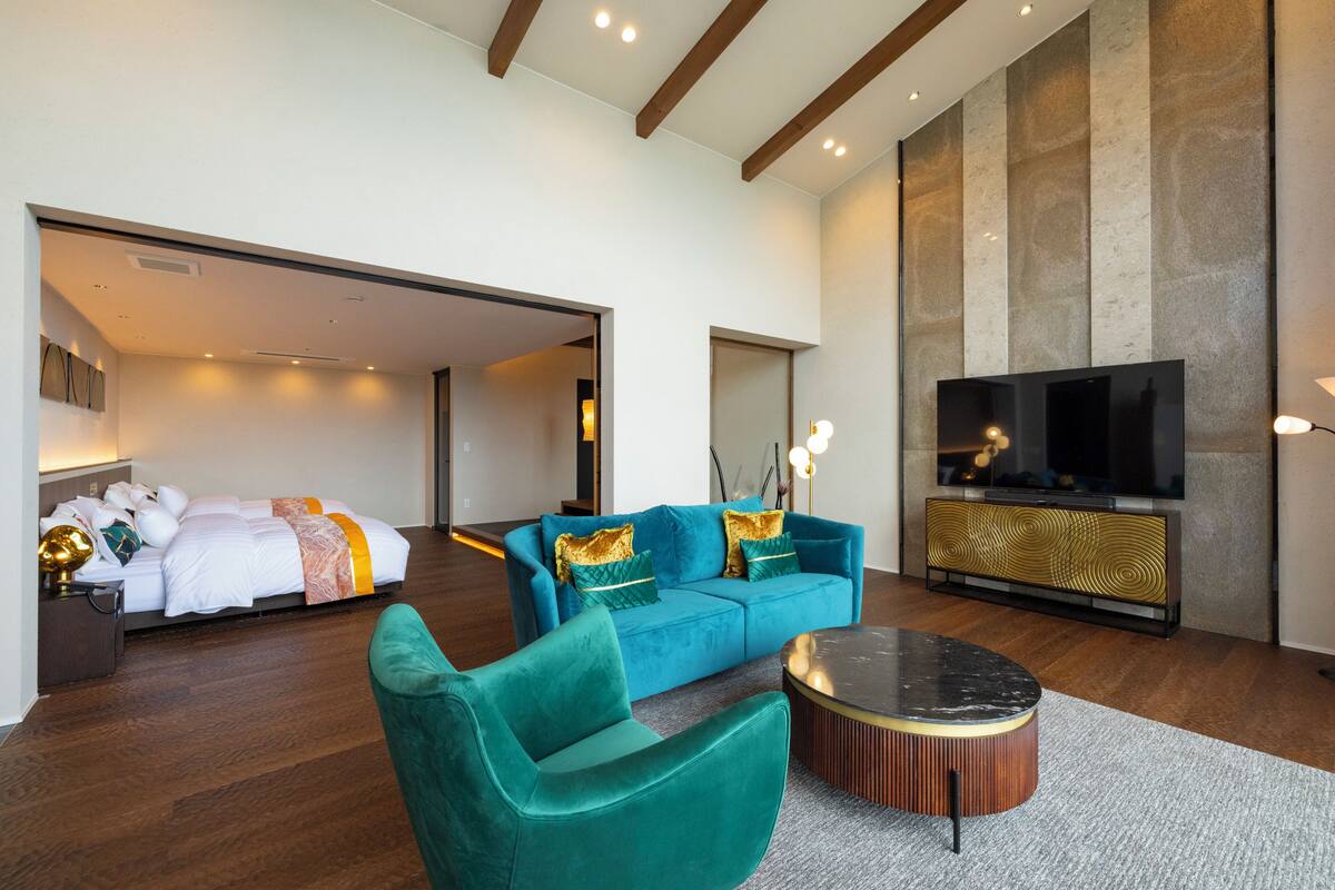 Una habitación de hotel moderna con una cama grande, un sofá azul, un televisor y un techo de madera.