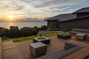 A modern outdoor deck with built-in seating and a fire pit, overlooking a body of water and a mountainous landscape. - Fuji Seiran (Numazu)