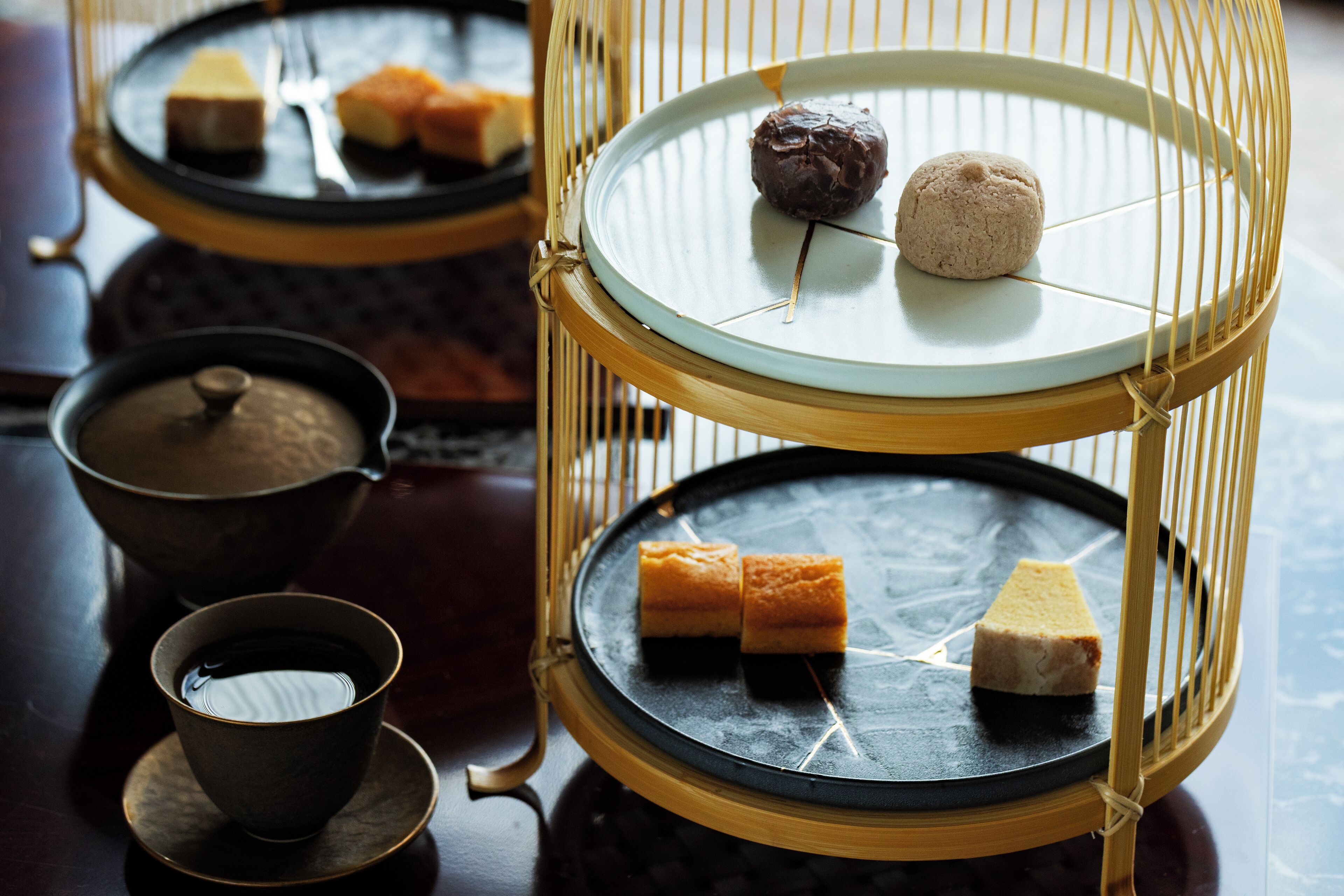 A traditional tea set with a teapot and cups, a wooden table, and a decorative tray with food items.