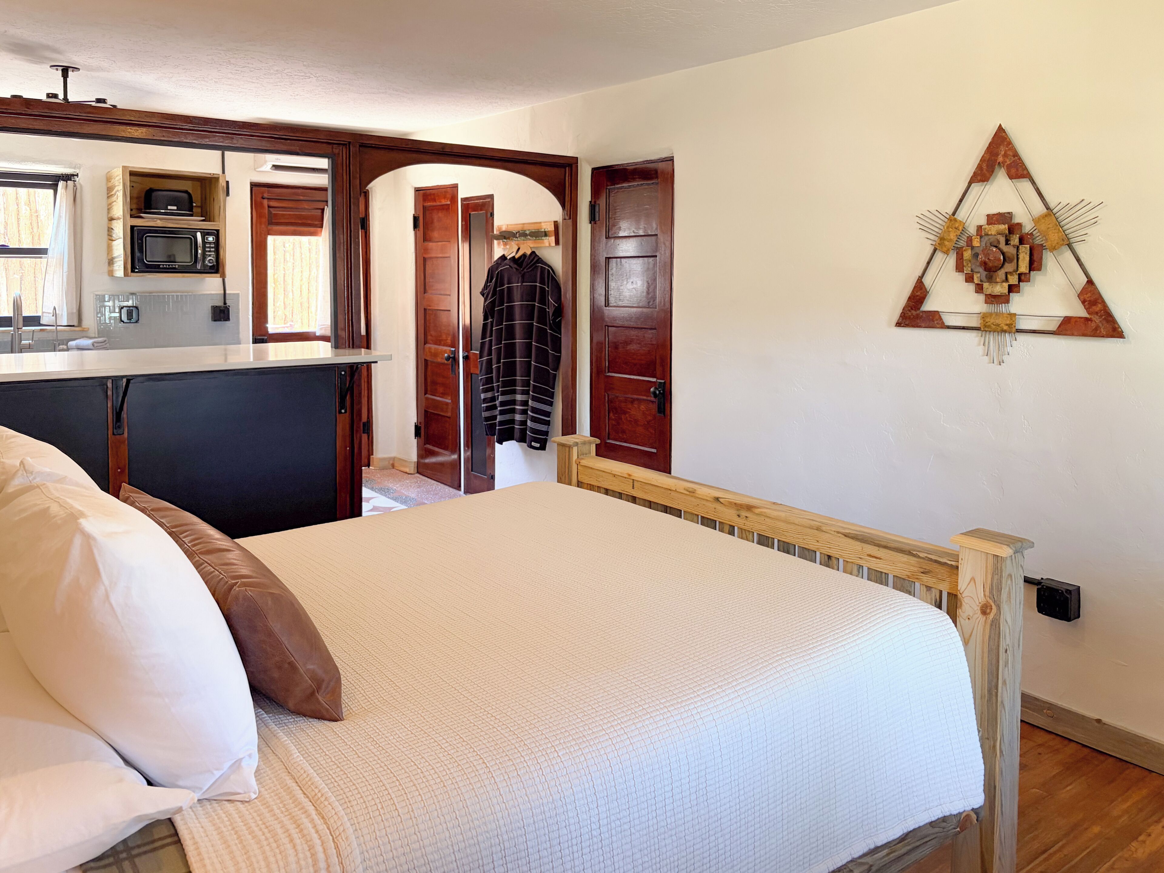 Ein Schlafzimmer mit einem Bett, einem Holz-Kopfteil, einem Wandbild und einem offenen Durchgang zu einer Küche.