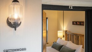 Habitación de hotel con cama, mesita de noche, lámpara y aplique de pared.