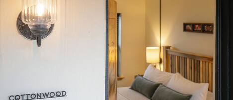 A hotel room with a bed, a nightstand, a lamp, and a wall-mounted light fixture.