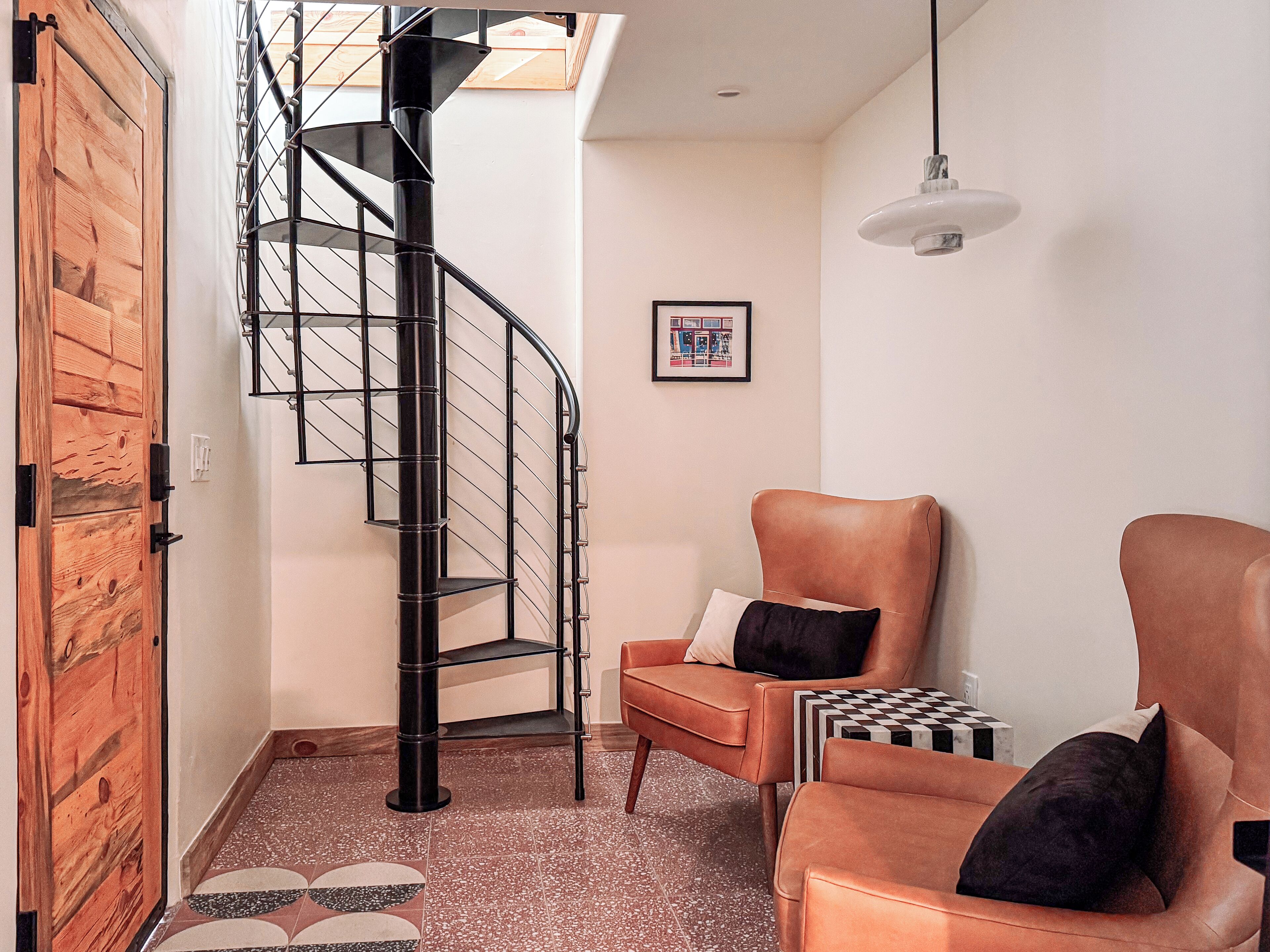 A modern living room with a spiral staircase, leather armchairs, and a checkered side table.