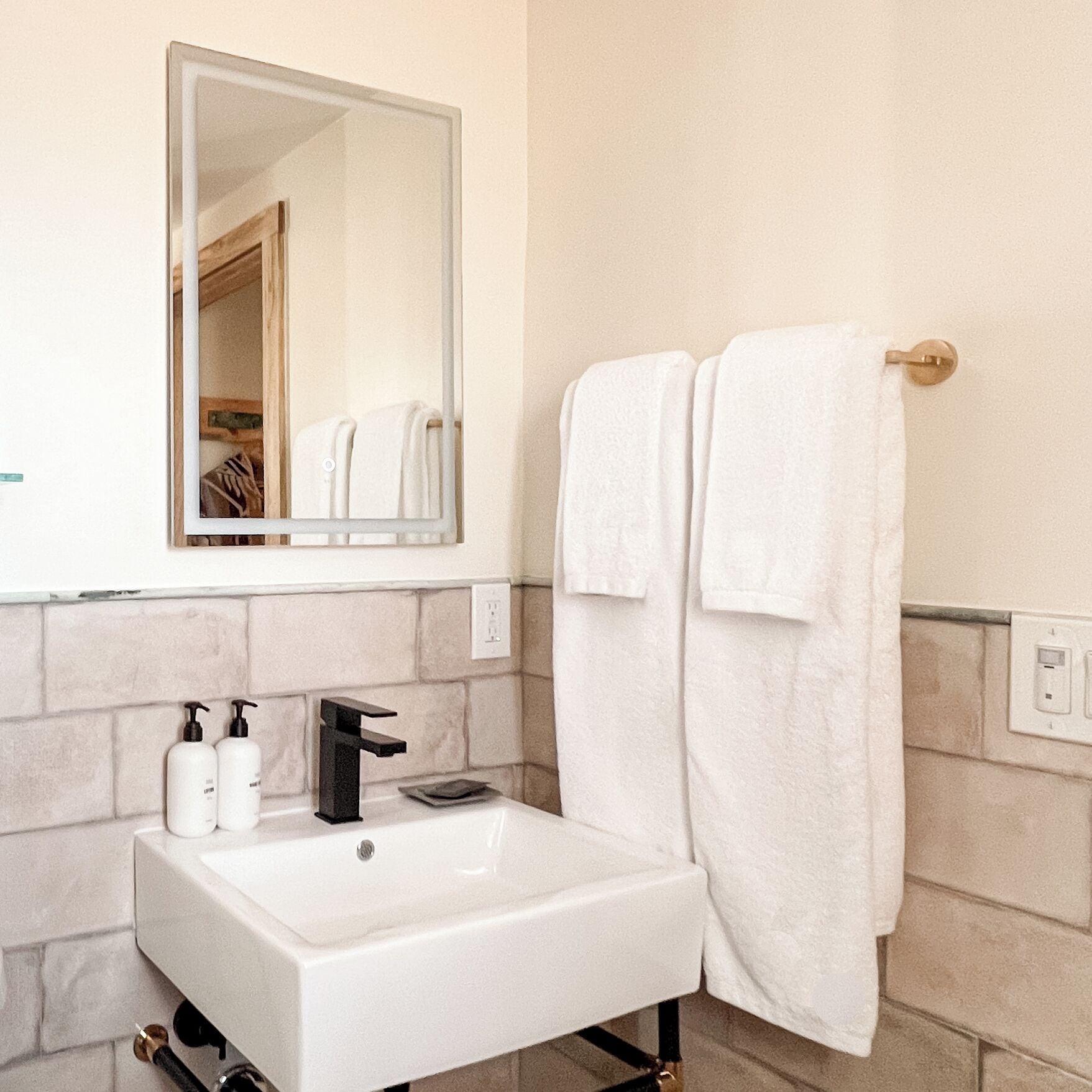 Un baño con un lavamanos blanco, un espejo y dos botellas de champú.
