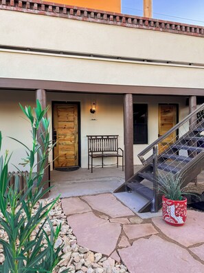 A building with a stone-paved entrance, a wooden bench, a metal staircase, and a potted plant. - Hoosier Hot Springs & Inn (Truth or Consequences)
