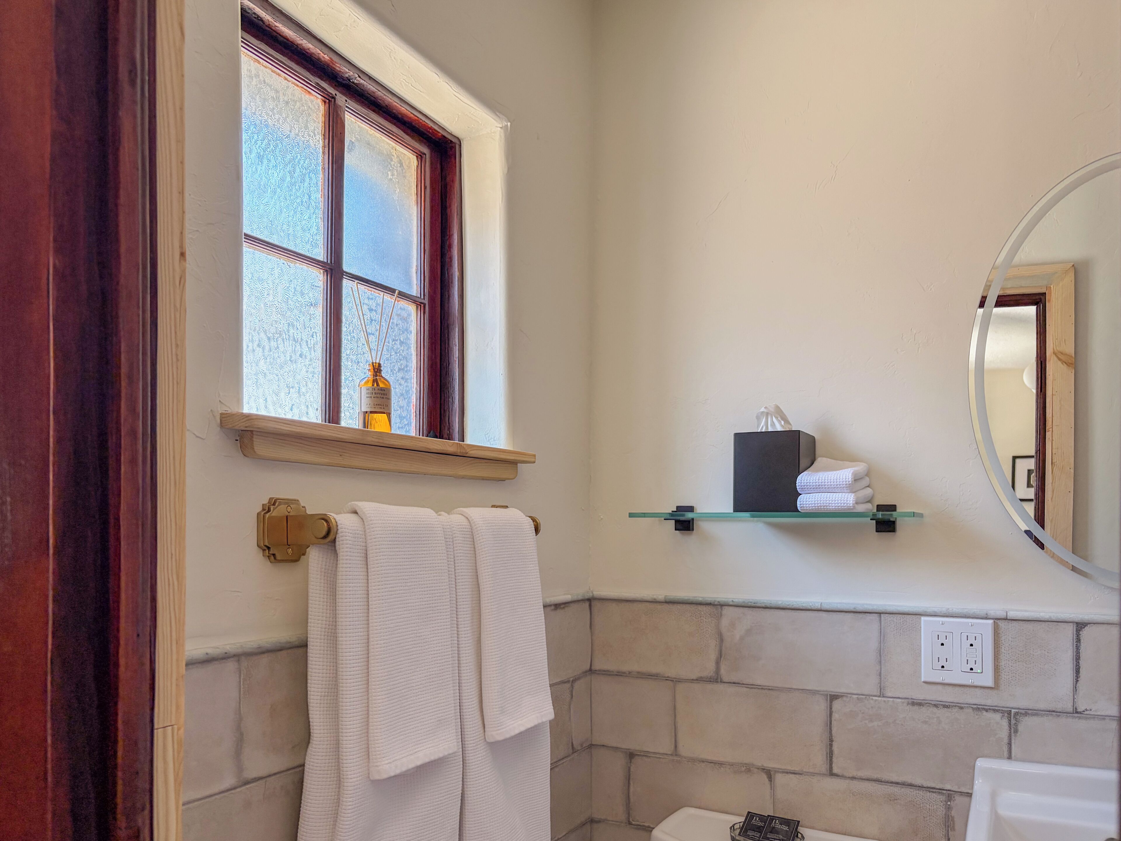 A bathroom with a window, a towel rack, a shelf with toiletries, and a toilet.