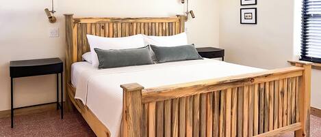 A wooden bed with a slatted headboard, a bedside table, a nightstand, and a wall-mounted air conditioner.