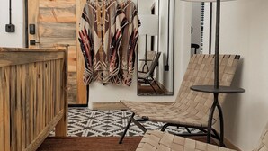 Una habitación moderna con puerta de madera, una silla de fibras naturales, alfombra estampada y un espejo grande.