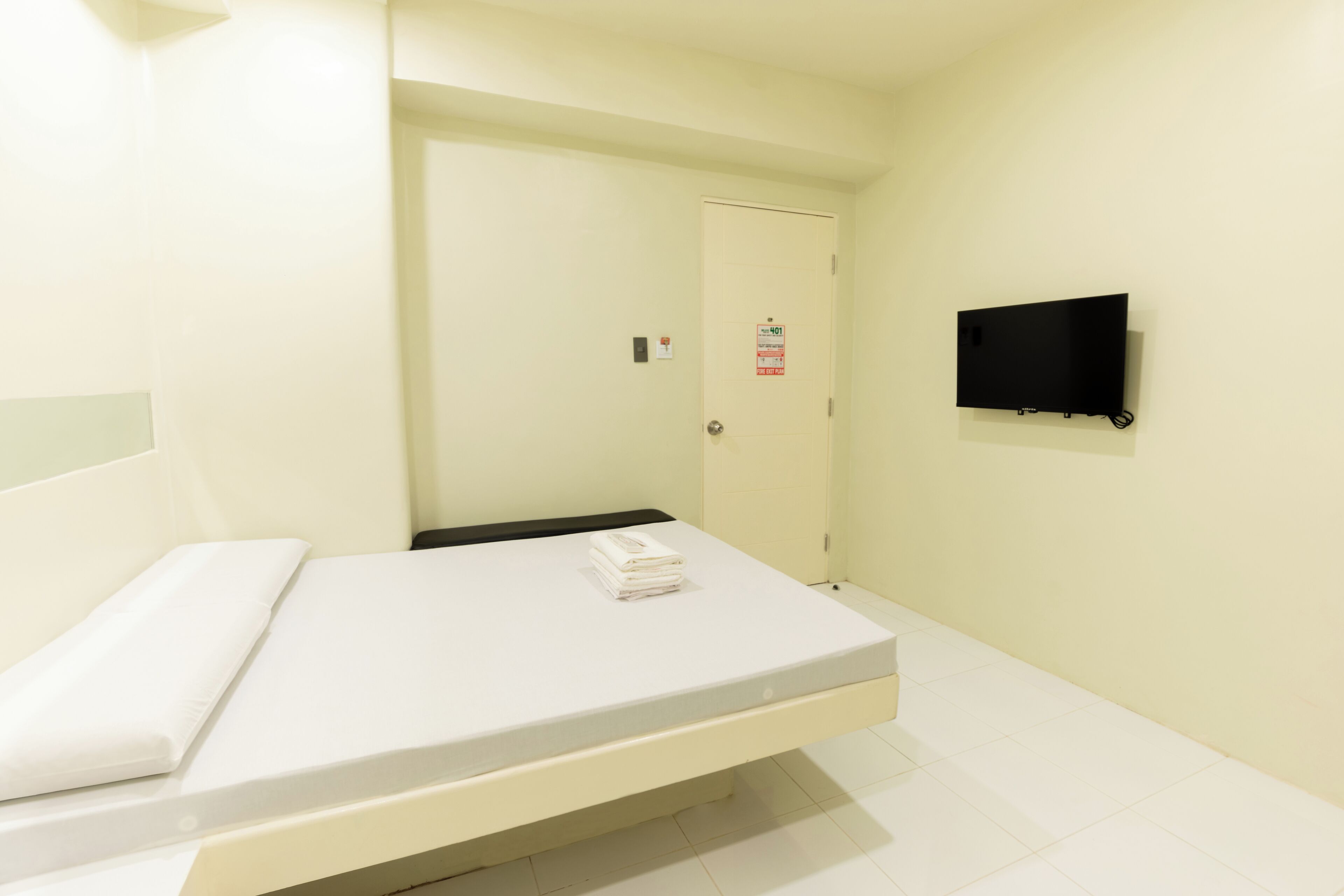 A hotel room with a bed, a television mounted on the wall, and a door with a sign.