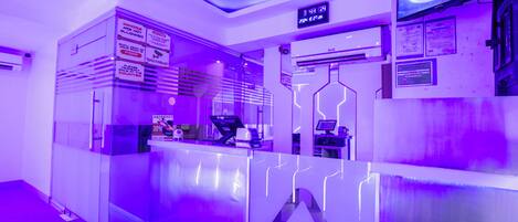 Uma área de recepção moderna com um relógio digital, uma luminária neon e um balcão de vidro.