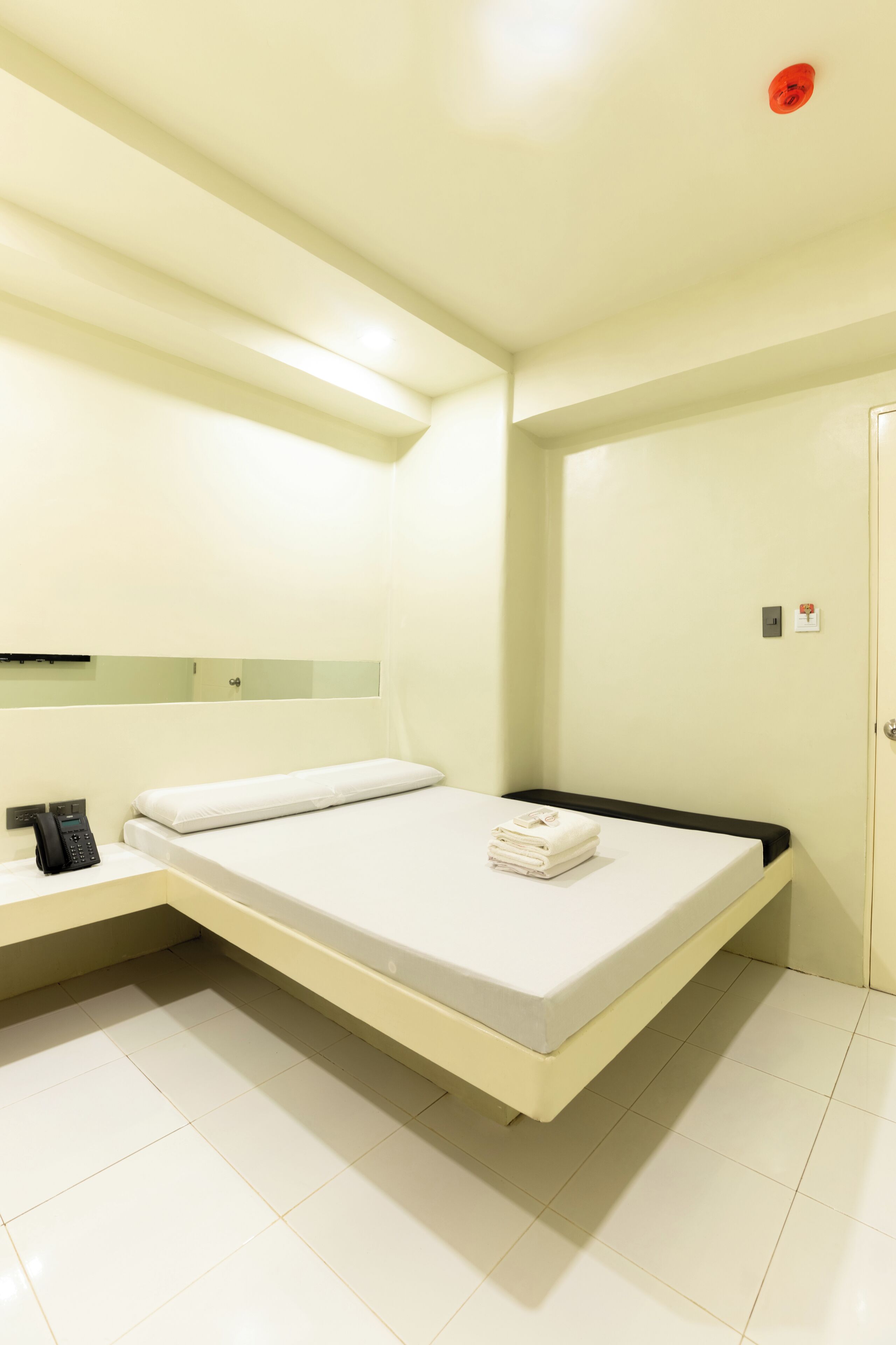 A hotel room with a bed, a bedside table with a phone, and a wall-mounted mirror.