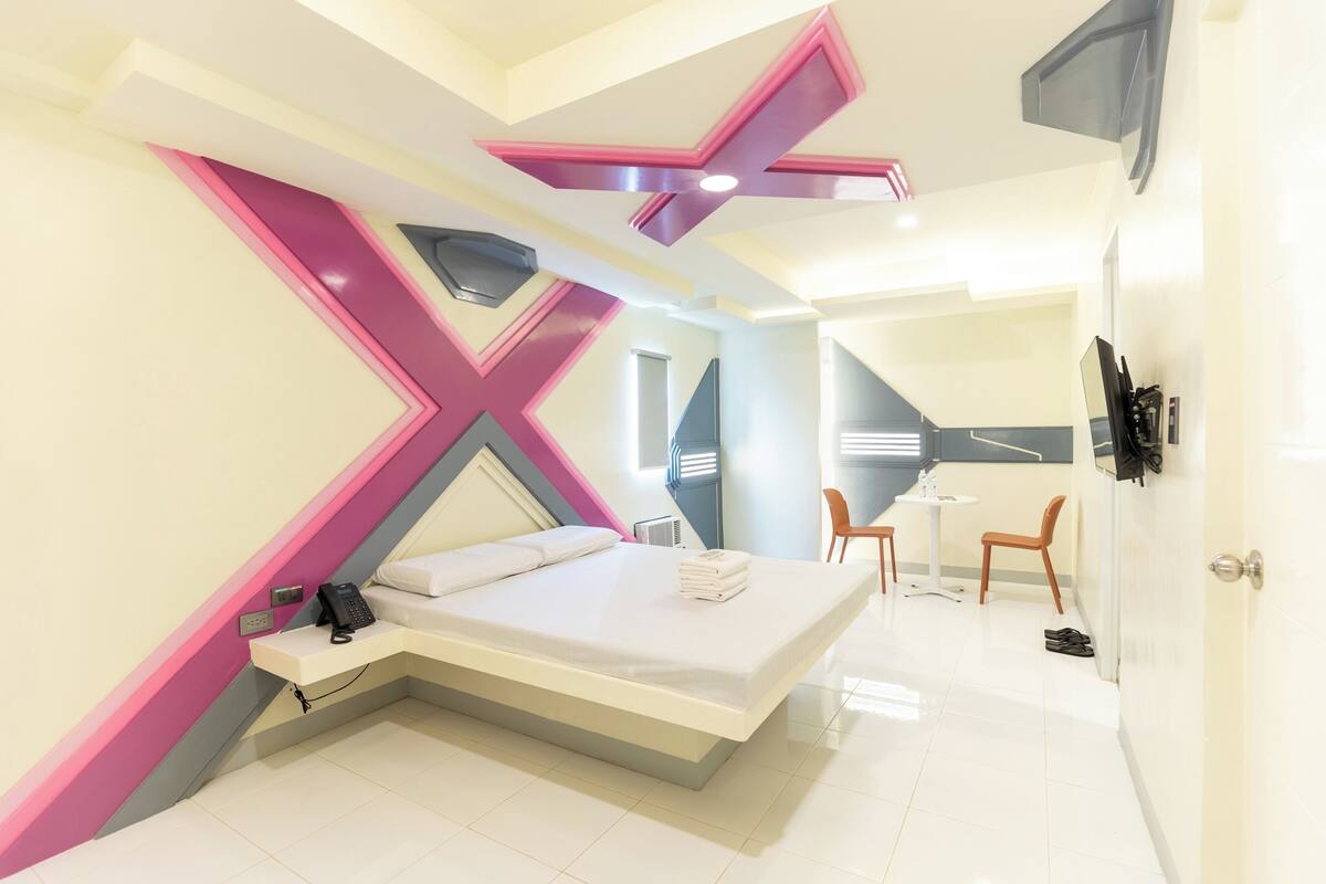 A modern hotel room with a bed, a desk, a chair, and a small table.