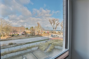 A view from a window overlooking a road with a pedestrian crossing, a building with a red roof, and leafless trees.