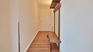 Ein schmaler Flur mit Holzdielen, einer Bank und einem an der Wand befestigten Regal mit Haken.