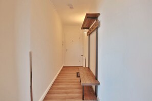 A narrow hallway with wooden flooring, a bench, and a wall-mounted shelf with hooks. - Seetempel Apartment 26 "Seehase" - Seetempel (Scharbeutz)