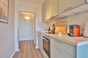 A modern kitchen with light wood cabinets, stainless steel appliances, and a countertop with a coffee machine and knife block. - Seetempel Apartment 26 "Seehase" - Seetempel (Scharbeutz)