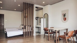 A modern hotel room with a bed, wooden floor, a dining area with a table and chairs, a mirror, and a potted plant. - Vinh Tuan Hotel (Xuan Huong - Da Lat)