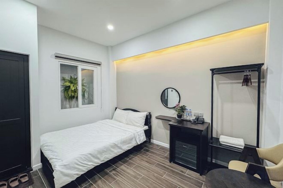 A bedroom with a bed, a bedside table, a mirror, a wardrobe, and a window.